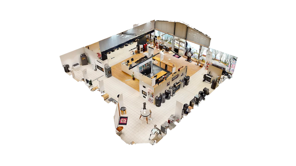 Intérieur lumineux d'un showroom d'environ 250 m² dédié aux systèmes de chauffage. Au premier plan, un homme d'âge mûr examine attentivement un poêle de masse contemporain exposé. L'espace est aéré, bien éclairé par la lumière naturelle. En arrière-plan, d'autres poêles (à bois et à granulés), des cheminées et des inserts sont présentés en situation réelle, certains intégrés dans des aménagements d'intérieur représentatifs. Un conseiller en chemise à proximité montre l'espace au client. L'atmosphère est professionnelle, chaleureuse et confiante, reflétant l'environnement où un client peut visualiser et découvrir les équipements avant de se décider.
